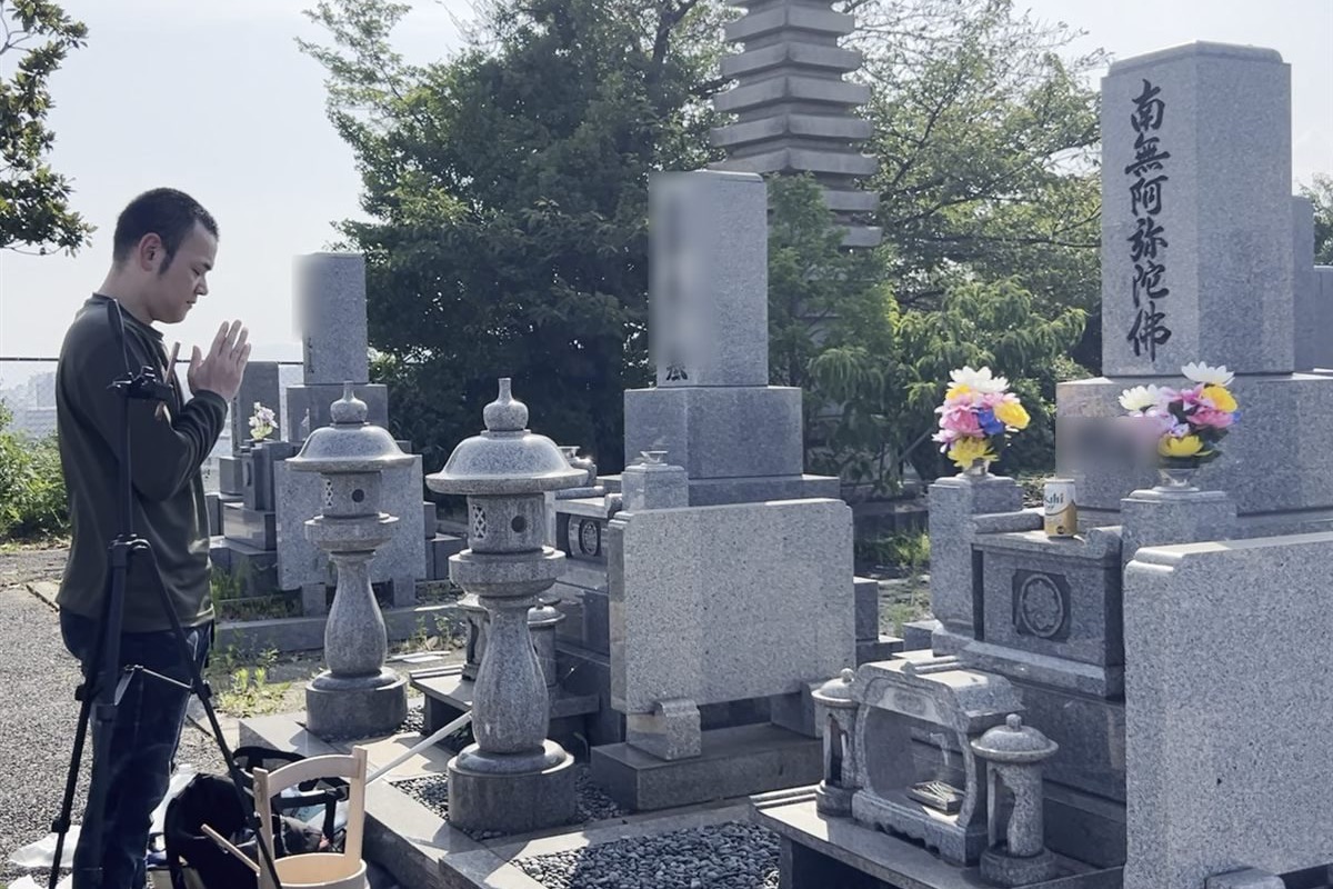 三脚に立てたスマホでご家族とつなぎ、墓前で手を合わせる代表